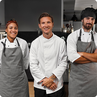 Group of three hospitality professionals in chef and waiter uniforms smiling